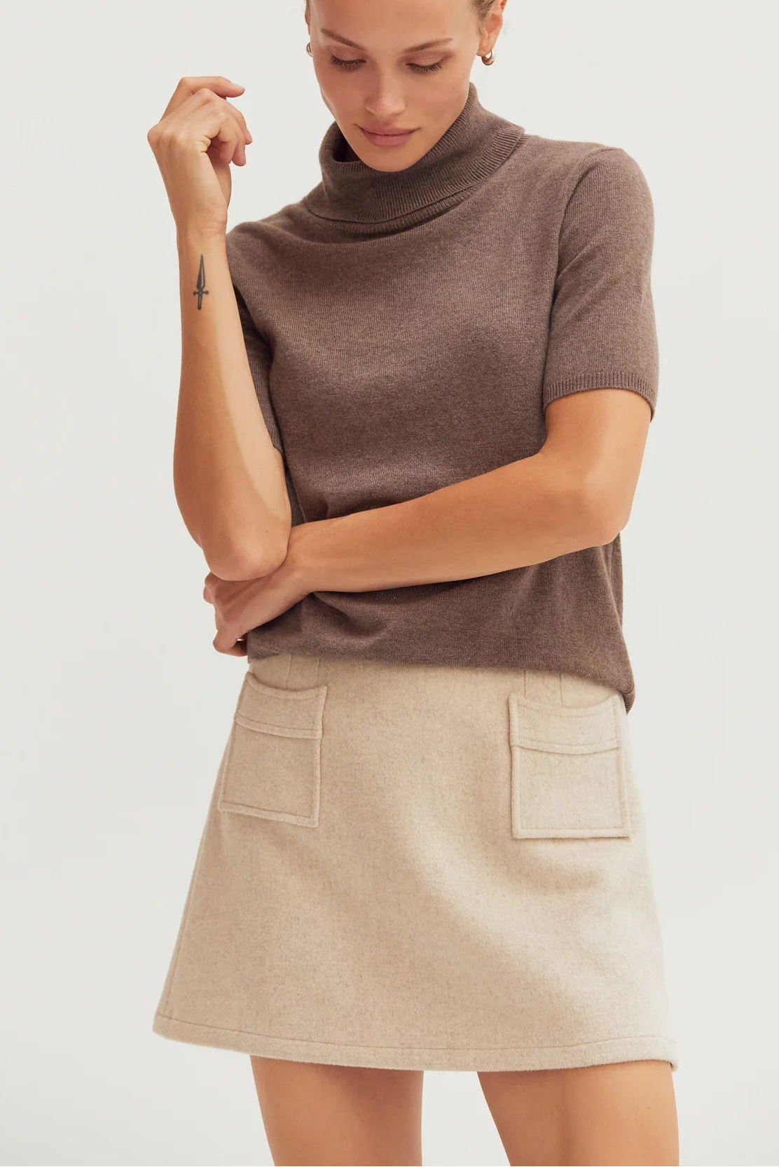 Woman wearing a brown turtleneck top and beige skirt on a white background
